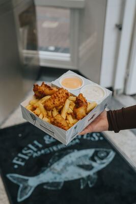 Fish & Fries box held above the branded doormat at the entrance