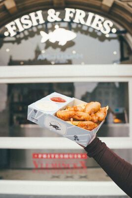 Fish & Fries box held up in front of the storefront with signage and Vleminckx branding